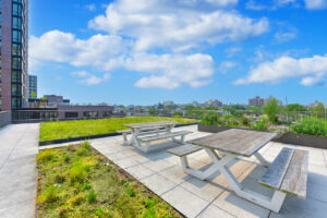 Rooftop picnic area, 2 tables, rooftop garden surrounding picnic area, skyline in the background.