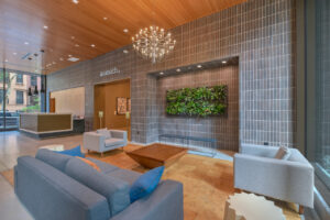 Interior Lobby, tile looking rug, loveseat and 2 lounge chairs, large contemporary coffee table, bench, Contemporary Front Desk, tiled walls, avanath signage above hallway.