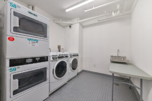 interior laundry facilities, gray tile floor, white walls, 2 dryers 2 washers, utility sink, table for folding clothes.