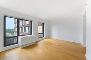 Interior Unit Living Room, ac unit in front of window, large floor to ceiling windows, wood floors, white walls.