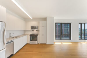 Interior Unit Kitchen, white cabinets, stainless steel appliances, large sink, floor to ceiling windows, wood floors.