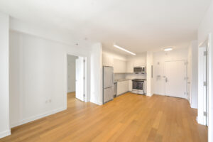 Interior Unit Living Room, open floor plan, stainless steel appliances, wood floors, stone countertop, white walls.